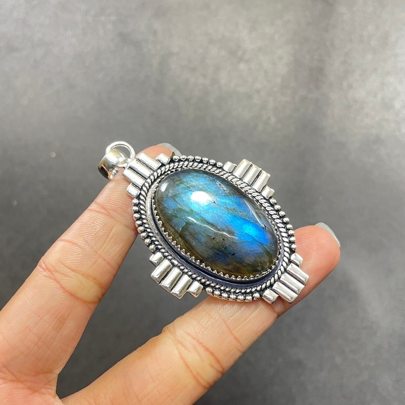 May include: A silver pendant featuring a large oval-shaped blue labradorite gemstone set in a silver bezel. The pendant has a detailed silver design around the stone and a silver bail.