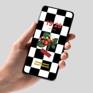 May include: A smartphone screen shows a black and white chequered pattern with a strawberry illustration and the text "always sweet never discreet." The time 19:26 is displayed in red. The phone is held in a hand.