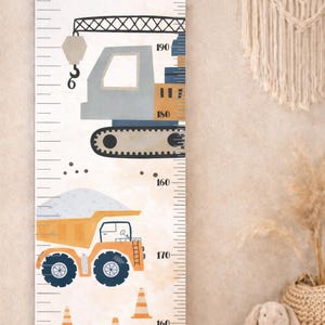 Peut inclure: Une toise pour enfants avec des véhicules de chantier. Le design comprend une grue, un camion benne et des cônes de signalisation dans des tons de gris, orange et bleu. La toise est montée sur une barre en bois et mesure jusqu'à 190 cm.