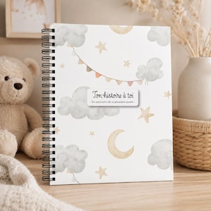 Peut inclure: Un journal à spirales avec une couverture blanche ornée d'illustrations à l'aquarelle de nuages, d'étoiles et d'un croissant de lune. Le texte "Ton histoire à toi" est affiché sur une étiquette blanche. Le journal est conçu pour enregistrer des souvenirs.