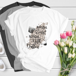 May include: White t-shirt with a graphic design featuring a leopard print, a glass of whiskey, and the text "Kinda Sweet Kinda Bit Dalton".