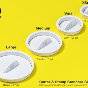 May include: Four white plastic cookie cutters in different sizes, labelled "XSmall", "Small", "Medium", and "Large". The cutters are shaped like a cat head with a small handle on the top. The cutters are on a yellow background. The text "Cookie Cat" is in the top left corner of the image. The text "Cutter & Stamp Standard Sizes" is at the bottom of the image. The text "(Please contact us for any queries, custom sizes or designs)" is below the text "Cutter & Stamp Standard Sizes".