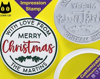 May include: White round Christmas cookie cutter with the text "With Love From Merry Christmas The Martins" in black and red lettering. The cutter is on a yellow background.