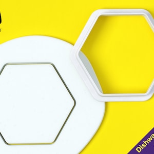 Puede incluir: Cortador de galletas hexagonal de plástico blanco sobre un fondo amarillo. El cortador es apto para lavavajillas.