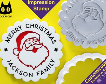 May include: A white plastic cookie cutter with a scalloped edge. The cutter is shaped like a circle with the words "Merry Christmas" and "Jackson Family" around the edge. A red and white Santa Claus head is in the centre of the cutter. The cutter is on a yellow background.