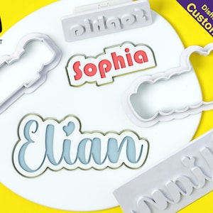 May include: Set of five white plastic cookie cutters with different names: Sophia, Elian, Olivia, and Birthday. The cutters are on a white surface with a yellow background. The cutters are dishwasher safe and customizable.