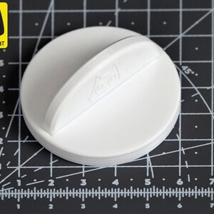 May include: White plastic bottle stopper with a handle. The stopper has a raised design on the top.