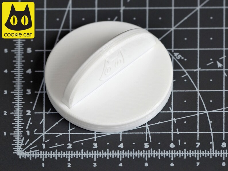 May include: White plastic bottle stopper with a handle. The stopper has a raised design on the top.