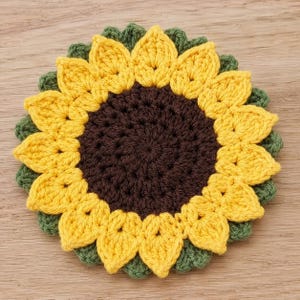 May include: A handmade crochet sunflower coaster. The coaster features a dark brown center, surrounded by yellow petals and a green outer edge. The sunflower design is a charming addition to any home decor.