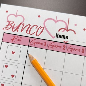 May include: A pink and white printable Bunco scorecard with a heart design. The scorecard has columns for Roll, Game 1, Game 2, Game 3, and Game 4. There is a space at the top for a name.