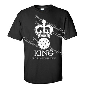 May include: Black t-shirt with a white design of a crown, a pickleball, and the text "KING OF THE PICKLEBALL COURT".