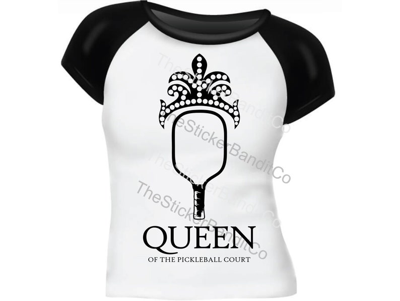 May include: A white t-shirt with black sleeves featuring a black and white illustration of a pickleball paddle with a crown on top. The text "QUEEN OF THE PICKLEBALL COURT" is printed below the paddle.