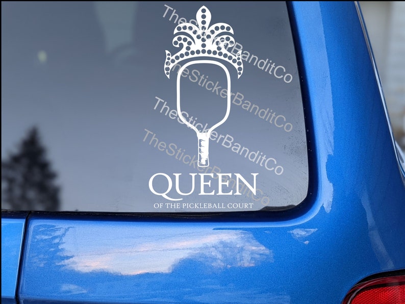 May include: White vinyl decal of a pickleball paddle with a crown on top. The text "QUEEN OF THE PICKLEBALL COURT" is below the paddle.