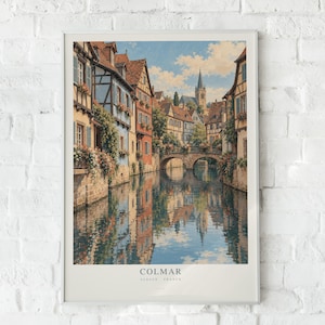 May include: A framed art print depicting a canal scene in Colmar, Alsace, France. The image features half-timbered houses with colourful facades, flower-filled balconies, and a stone bridge over the water. The text COLMAR ALSACE FRANCE is at the bottom.