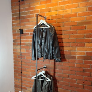 Industrial wall mounted clothes rack made of a steel pipe and joints, screwed to a red brick wall. It has two hangers of the selected length. Hanging jackets display / looks very nicely.