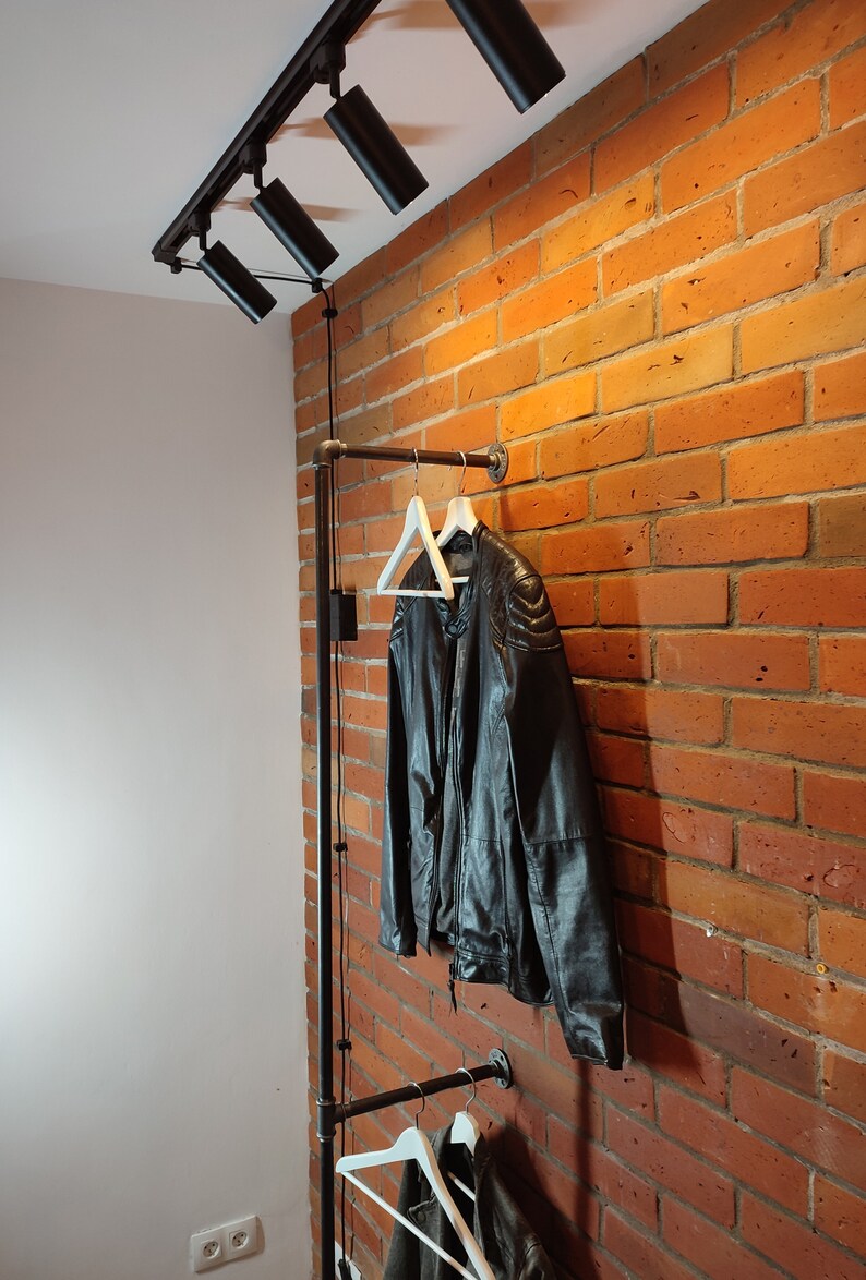 Industrial wall mounted clothes rack made of a steel pipe and joints, screwed to a red brick wall. It has two hangers of the selected length. Hanging jackets display very nicely.