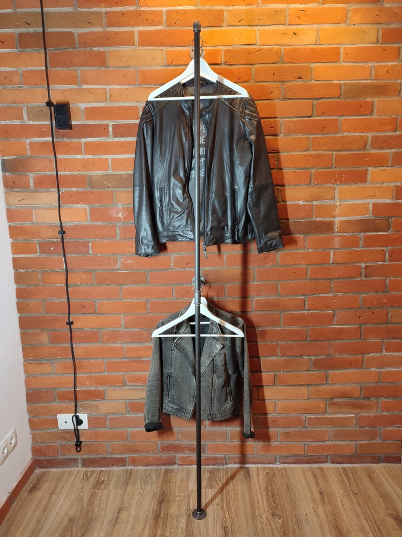 Industrial wall mounted clothes rack made of a steel pipe and joints, screwed to a red brick wall. It has two hangers of the selected length. Hanging jackets display very nicely.