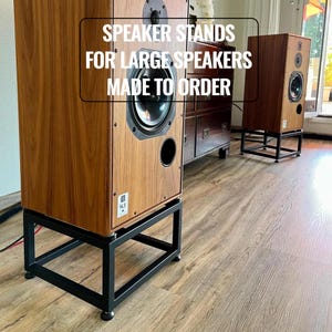 May include: Wooden speakers on black metal speaker stands. The speakers have a dark wood grain finish and are mounted on black, geometric stands. The text on the image reads: "SPEAKER STANDS FOR LARGE SPEAKERS MADE TO ORDER."
