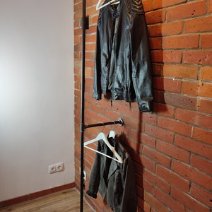 Industrial wall mounted clothes rack made of a steel pipe and joints, screwed to a red brick wall. It has two hangers of the selected length. Hanging jackets display / looks very nicely.