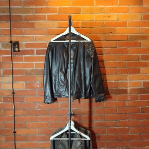 Industrial wall mounted clothes rack made of a steel pipe and joints, screwed to a red brick wall. It has two hangers of the selected length. Hanging jackets display very nicely.