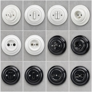 May include: A collection of twelve circular wall-mounted electrical components, including light switches, power outlets, and data ports. The set features six white and six black glossy ceramic-style fixtures with visible mounting screws.