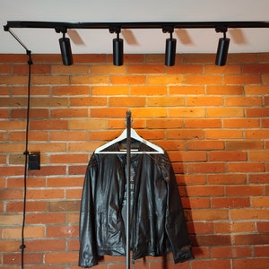 Industrial wall mounted clothes rack made of a steel pipe and joints, screwed to a red brick wall. It has two hangers of the selected length. Hanging jackets display very nicely.