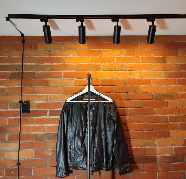 Industrial wall mounted clothes rack made of a steel pipe and joints, screwed to a red brick wall. It has two hangers of the selected length. Hanging jackets display very nicely.