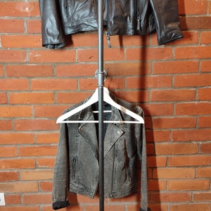 Industrial wall mounted clothes rack made of a steel pipe and joints, screwed to a red brick wall. It has two hangers of the selected length. Hanging jackets display very nicely.