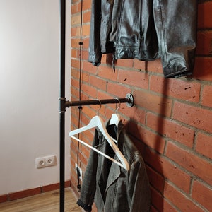 Industrial wall mounted clothes rack made of a steel pipe and joints, screwed to a red brick wall. It has two hangers of the selected length. Hanging jackets display very nicely.