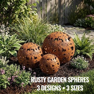 May include: Three rusty metal garden spheres with floral cut-out designs in varying sizes. The spheres are displayed in a garden setting with lush greenery and the text "RUSTY GARDEN SPHERES 3 DESIGNS • 3 SIZES".