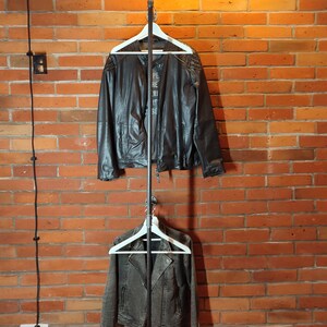 Industrial wall mounted clothes rack made of a steel pipe and joints, screwed to a red brick wall. It has two hangers of the selected length. Hanging jackets display very nicely.