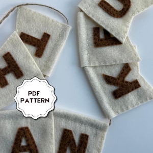 May include: A felt banner featuring off-white pennants with brown stitched letters spelling out THANK YOU. The pennants are connected by a thin twine string. A white scalloped label with the black text PDF PATTERN is overlaid on the image.
