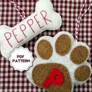 May include: Two felt dog ornaments. One is a white bone shape with the name "PEPPER" embroidered in red. The other is a paw print with brown pads and a red "P". Both have red and white string for hanging.