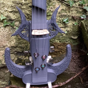 Puede incluir: Un violín eléctrico negro con un diseño único y futurista. El violín tiene un cuello azul y detalles intrincados y curvos en el cuerpo.