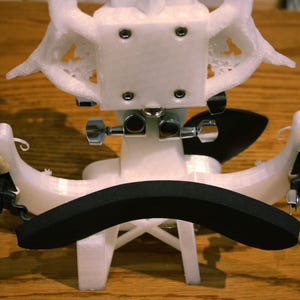 May include: White 3D printed violin shoulder rest with a black foam pad. The shoulder rest has two adjustable arms with metal screws.