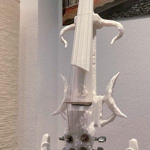 Puede incluir: Un viol&iacute;n el&eacute;ctrico blanco con un dise&ntilde;o org&aacute;nico &uacute;nico. El viol&iacute;n tiene un cuerpo tallado y texturizado y un reposacabezas negro.