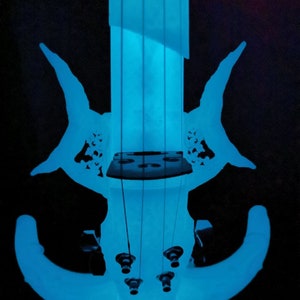 May include: A blue electric violin with a unique design. The violin has a futuristic look with a curved body and a long neck. The strings are visible and the tuning pegs are at the top of the neck.