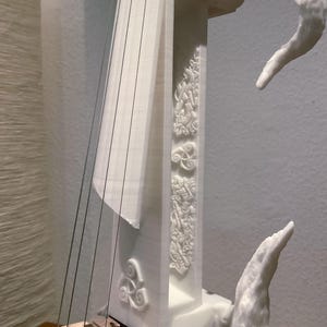 Puede incluir: Viol&iacute;n blanco impreso en 3D con detalles intrincados y un puente de madera. El viol&iacute;n tiene un dise&ntilde;o &uacute;nico con un cuello curvo y un remate decorativo.