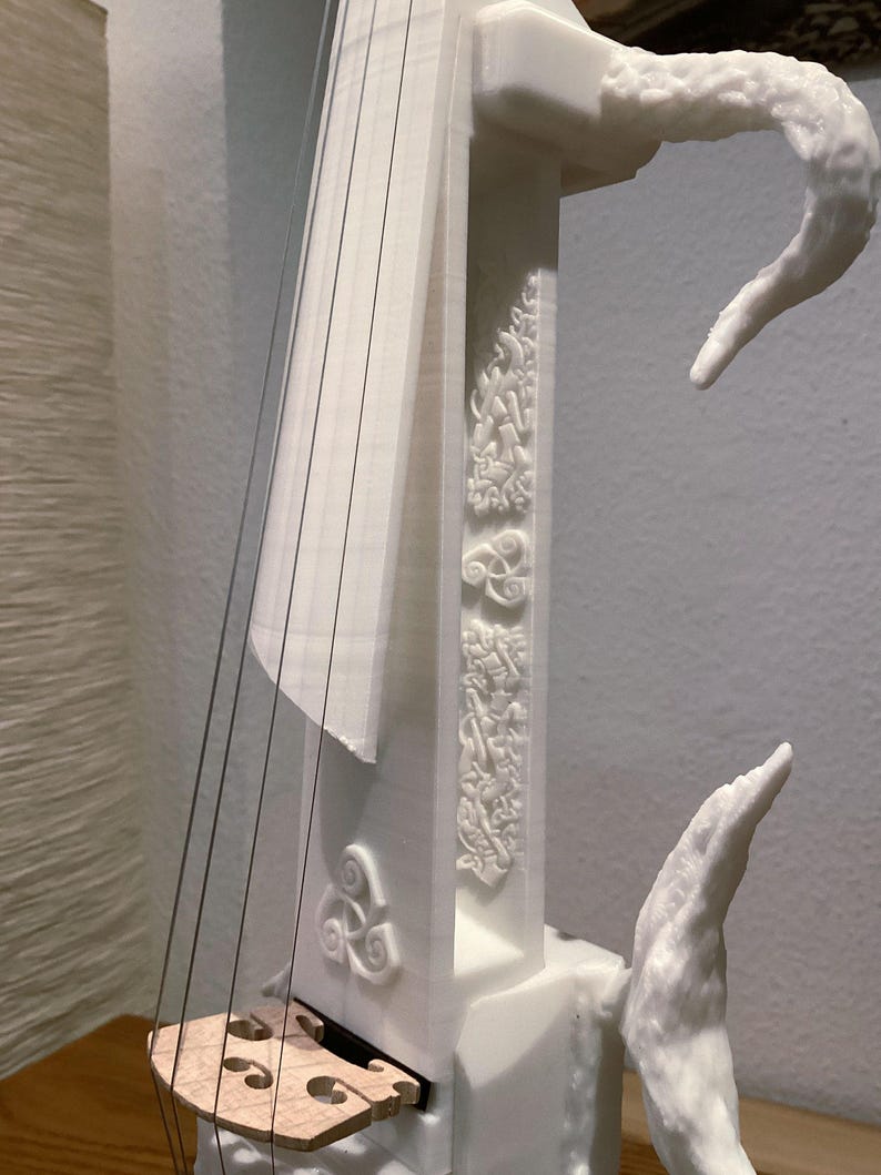 Puede incluir: Viol&iacute;n blanco impreso en 3D con detalles intrincados y un puente de madera. El viol&iacute;n tiene un dise&ntilde;o &uacute;nico con un cuello curvo y un remate decorativo.