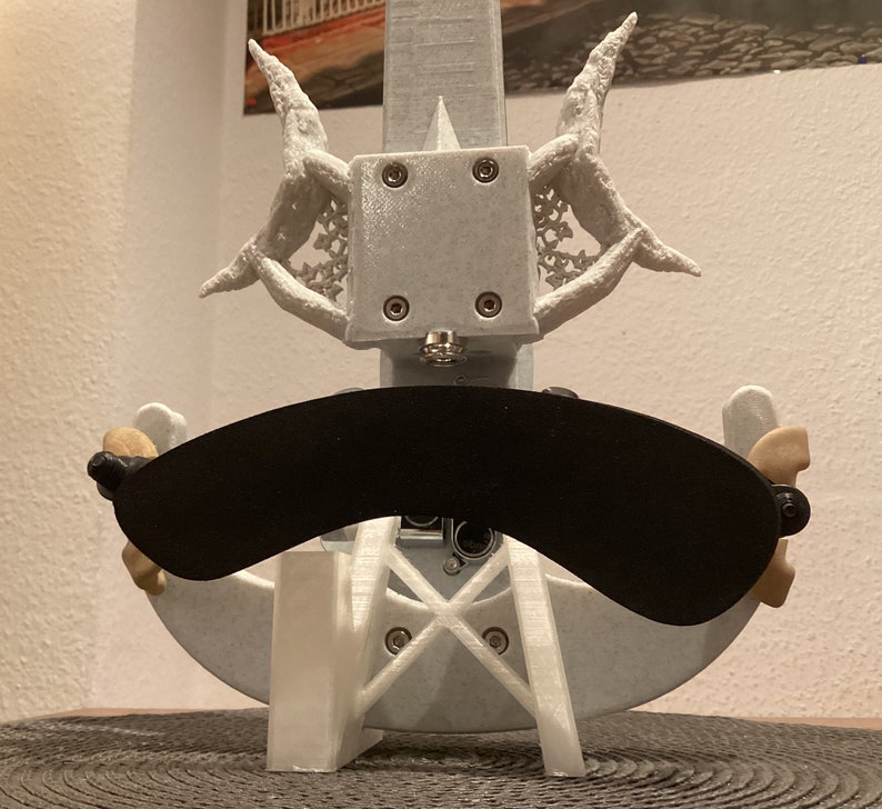 K&ouml;nnte beinhalten: Ein wei&szlig;er 3D-gedruckter Geigenst&auml;nder mit einem schwarzen, gebogenen Schalld&auml;mpfer. Der St&auml;nder hat ein dekoratives Design mit filigranen Details.