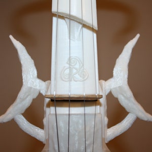 Puede incluir: Viol&iacute;n blanco impreso en 3D con detalles intrincados y un dise&ntilde;o de nudo celta en el cuello. El viol&iacute;n tiene dos alas curvas a cada lado del cuello.