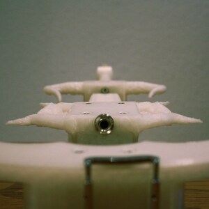 May include: White plastic object with a round hole in the center and two curved arms on either side. The object is designed to hold something in place.