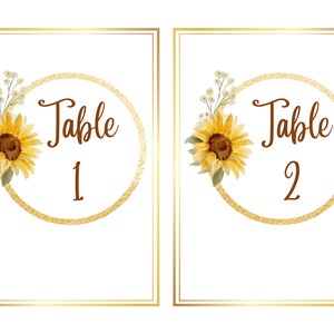 May include: Two table number cards with a gold circle and sunflower design. The text on the cards reads "Table 1" and "Table 2".