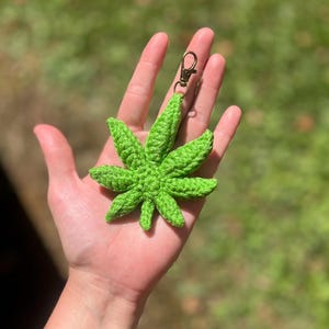 May include: A green crocheted marijuana leaf keychain with a gold metal clasp.