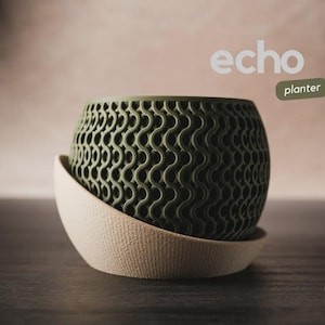 May include: A green, patterned planter with a matching saucer. The planter has a unique wave-like design and the word "echo" is displayed above it. The word "planter" is also displayed. The planter is sitting on a dark surface.