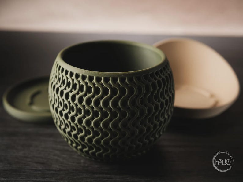 Puede incluir: Una maceta esf&eacute;rica de color verde oliva con un patr&oacute;n de celos&iacute;a ondulado repetitivo en su exterior. La maceta tiene una parte superior abierta y se acompa&ntilde;a de una base circular a juego en verde oliva y un cuenco de color beige claro.