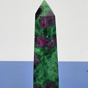 May include: A tall, polished gemstone obelisk. The stone features a vibrant green base colour with irregular patches of deep magenta and black. The obelisk has a pointed top and a rectangular base.