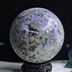 Könnte beinhalten: Eine große, polierte Kugel aus violettem und grünem Achat auf einem schwarzen Holzsockel. Die Kugel hat eine natürliche, unregelmäßige Öffnung.