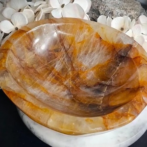 Könnte beinhalten: Eine große, ovale Schale aus klarem Quarz mit braunen und goldenen Einschlüssen. Die Schale ist glatt und poliert und hat einen leicht schillernden Glanz.