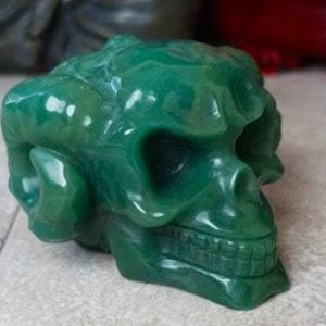Może przedstawiać: Zielona czaszka z jadeitu z rogami, rzeźbiona w szczegółach. Czaszka jest wypolerowana i ma gładkie, błyszczące wykończenie.